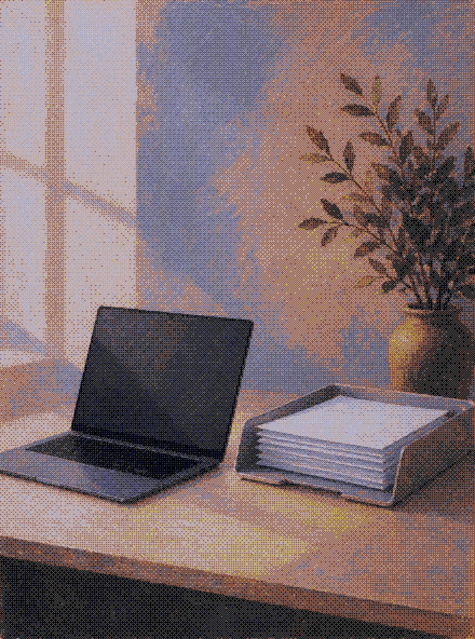 a laptop beside a full paper tray on a desk in the afternoon light